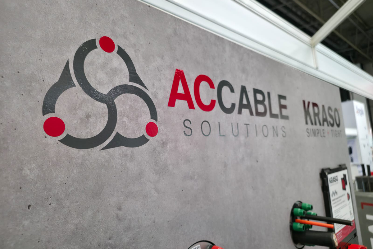 AC Cable Solutions and KRASO logos on exhibition wall with cable duct sealing display in foreground at Solar & Storage trade show.