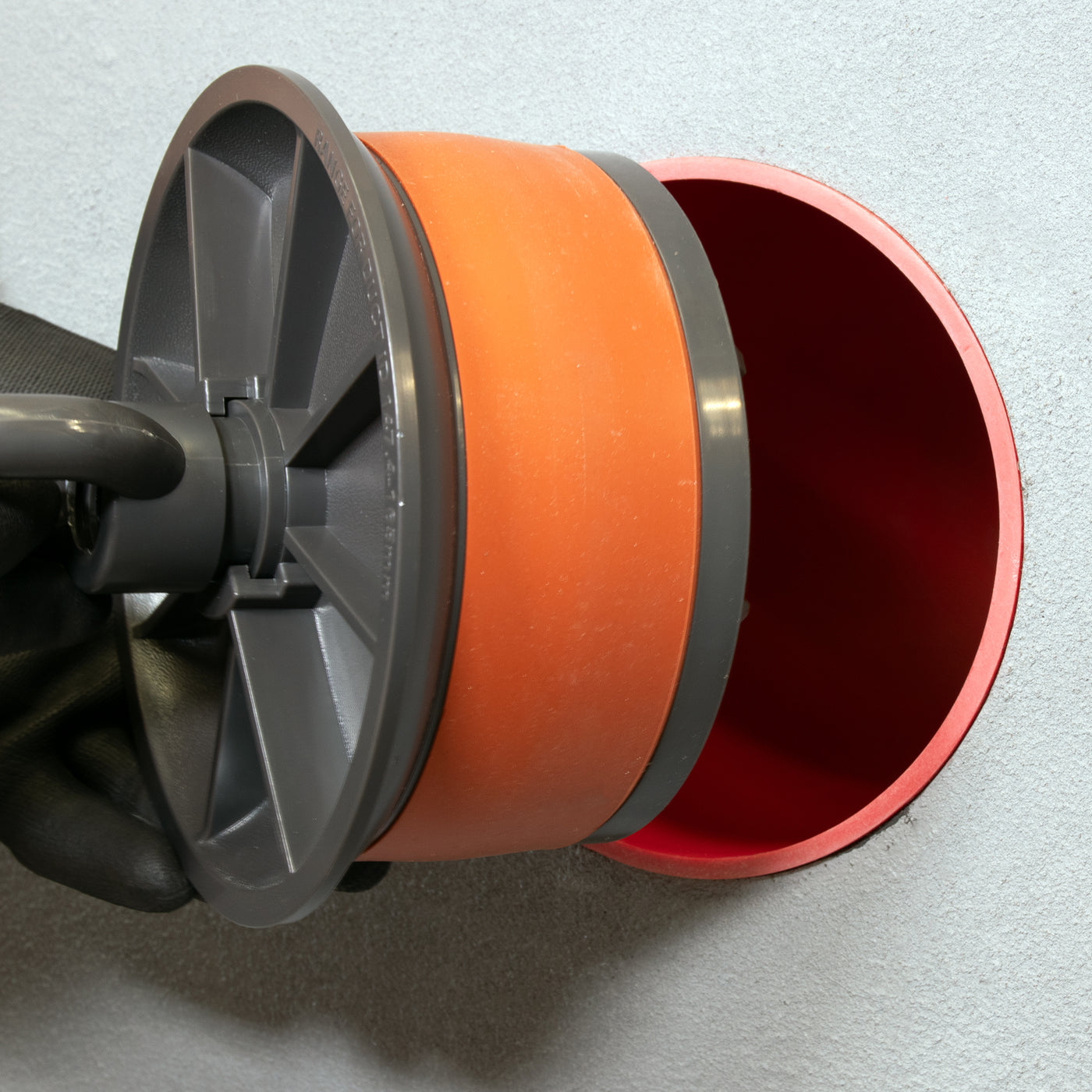 Installing DuctSeal expandable duct plug into orange PVC conduit, gloved hand tightening handle for mechanical blanking and temporary sealing